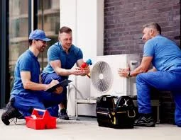 Three HVAC technicians discussing an outdoor air conditioning system